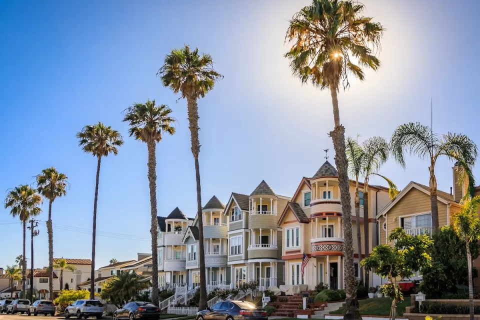 Historic Victorian homes in Huntington Beach, California with tall palm trees on a sunny day.
